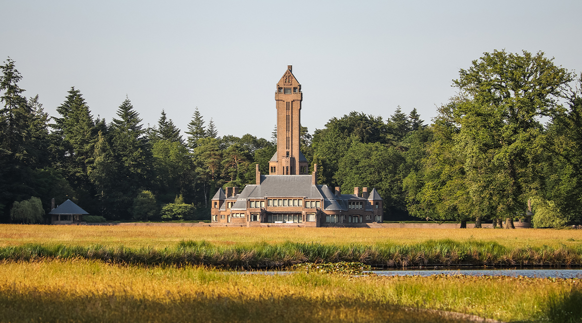 A unique Dutch building with a large tower and country house with yellow grass in the foreground